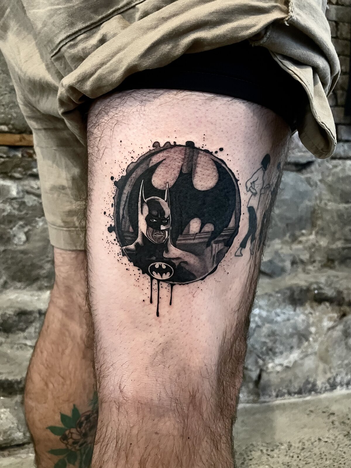 Black and grey Batman tattoo with bat signal emblem on a thigh